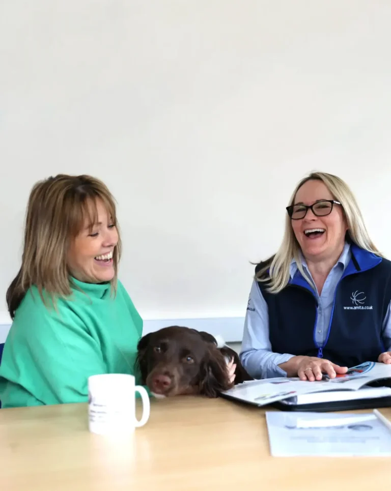 Jeanette and Mandy laughing at a desk with the dog